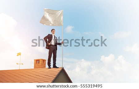 Businessman standing on house roof and holding white flag. Mixed media