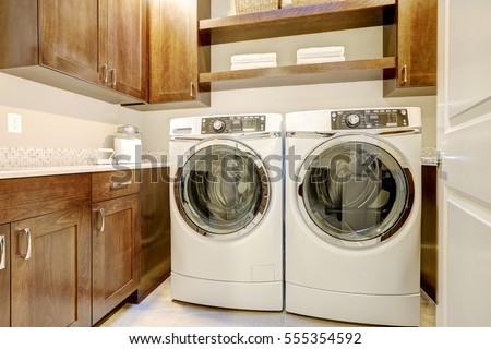 White and brown laundry room features modern appliances placed under shelves and cabinets. Northwest, USA

