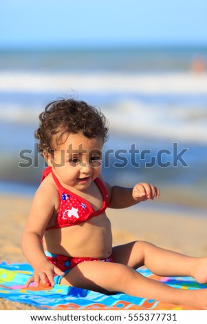 Baby girl on the beach seated on a towel