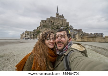 beautiful couple taking a selfie in front of Mont Saint Michel. France.