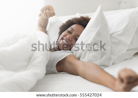 Beautiful woman waking up in her bed, she is smiling and stretching Royalty-Free Stock Photo #555427024