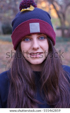 Portrait of a young caucasian woman with blue eyes dressed in a wool cap with a white space where you can add information. She is in the field on an autumn day. 