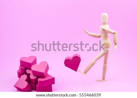 Wooden dummy are kicking paper box red heart shape to a pile of paper box red heart shape on pink background with copy space for your text.Concept Valentine's Day, Day of love.