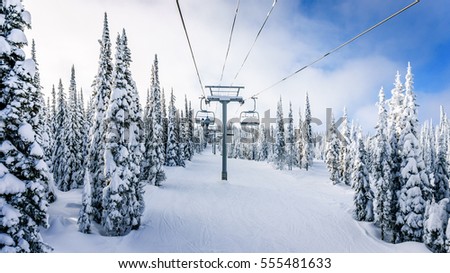 Riding the Chair Lift through the Forest of the High Alpine with Snow Covered Trees on the Hills surrounding Sun Peaks Village in the Mountains of the Shuswap Highlands of British Columbia Royalty-Free Stock Photo #555481633