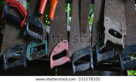 Many old hand saws hanging from a rack on the wall.                        