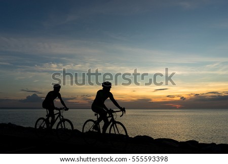 Silhouettes of Cyclists on bicycle at the ocean in the sunset scene