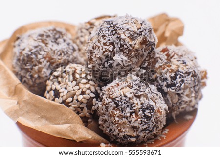 Chocolates are handmade in coconut flakes and sesame seeds in a pot on a white background