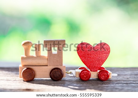 Red Heart Shape with Wooden Toy Train on wooden floor over blurred green garden  background,Image to Valentine Day concept.