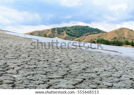 Cracked slope with mud volcano and cloudy sky. Dry land in natural park with muddy volcanoes, dramatic landscape, unique geological phenomenon in Europe.