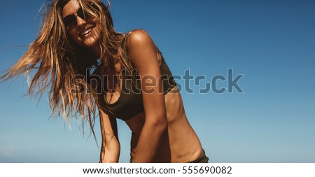 Portrait of attractive young woman in bikini against blue sky with fluttering hair. Female model having fun outdoors.