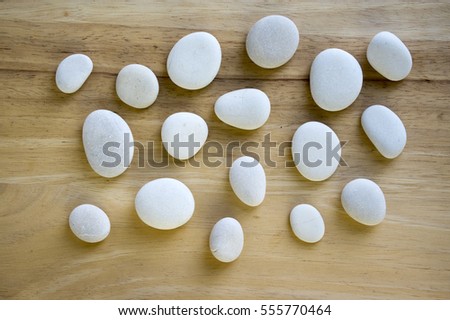 White pebbles on wooden background, simplicity, daylight, space around stones, one by one