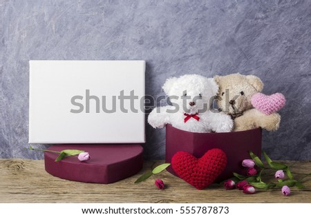 Love concept of teddy bear in red heart gift box on wood table and blank canvas frame for valentines day and wedding