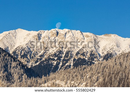 Winter scenery in the mountains, with snow covered peaks and setting moon
