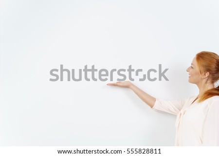 One woman in a pretty blouse and with red hair extends hand with palm side up against a blank white board