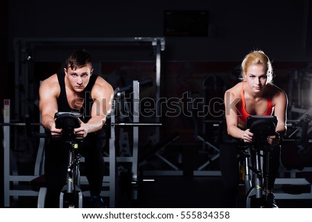 Sporty couple exercising at the fitness the exercise bike on a dark background at gym. Royalty-Free Stock Photo #555834358