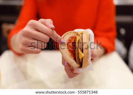 Girl holding a bitten off a piece burger in one hand. Girl with delicious tasty fast food cheeseburger and shows a finger at him. The concept of fast food. Tasty unhealthy Burger sandwich in hands, 