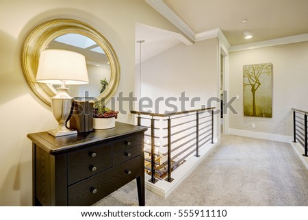 Second floor landing with black console table topped with a lamp placed under round gold mirror. Northwest, USA