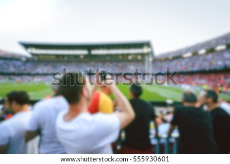 Blurred crowd of spectators and a man taking picture on stadium at a sporting event