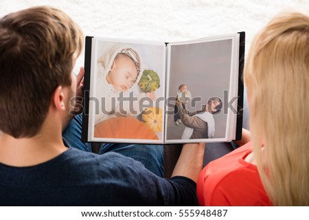 High Angle View Of Young Couple Looking At Photo Album