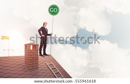 Young caucasian businessman standing on house roof presenting green construction. Mixed media