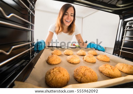 Young Happy Woman Baking Fresh Cookies In Oven At Kitchen Royalty-Free Stock Photo #555962092