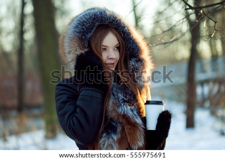 Young and attractive woman on walk, winter, warm coat with a hood, coffee to go