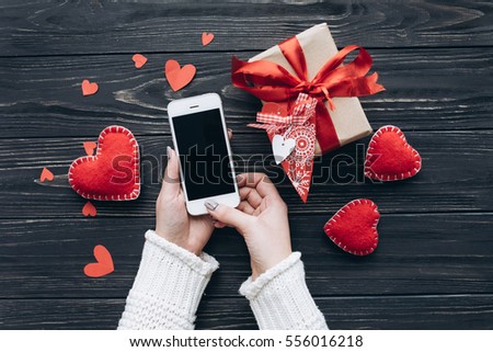 Female hands writing sms on smart phone for Valentine's day, gifts and toy red hearts.