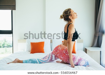 Woman doing yoga exercise on bed at home. Morning workout in bedroom. Healthy and sport lifestyle. Royalty-Free Stock Photo #556016467