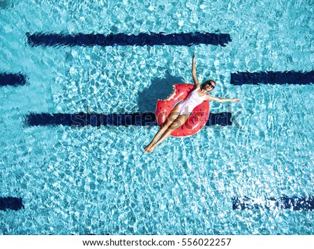 Woman relaxing on donut lilo in the pool water in hot sunny day. Summer holiday idyllic. Top view. Royalty-Free Stock Photo #556022257