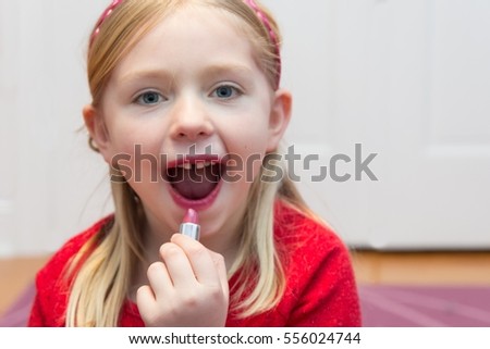 adorable school age girl putting on lipstick