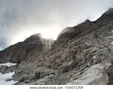 Steep north side of Mount Robie Reid rocky massif with summer sun shining through clouds, Garibaldi Ranges, Mission, British Columbia, Canada Royalty-Free Stock Photo #556071304