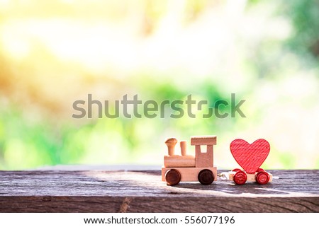 Red Heart Shape with Wooden Toy Train on wooden floor over blurred green garden  background,Image to Valentine Day concept.