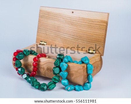 Picture of the opened light-coloured box for bijouterie with turquoise, malachite and coral bead necklaces isolated on white background. Handmade carved jewel box with beads. Side view.