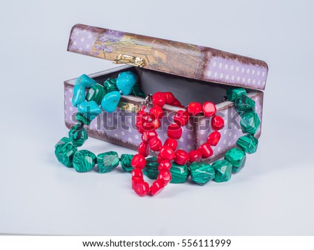 Picture of the opened purple-coloured box for bijouterie with turquoise, malachite and coral bead necklaces on white background. Handmade decoupage jewel box. Side view.