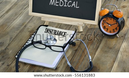 notebook with the words "INSURANCE" and stethoscope, glasses, chalk board, alarm clock on a wooden table. medical and health care concept.