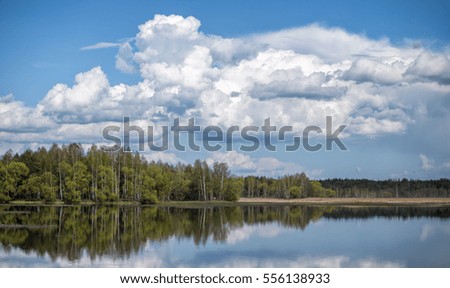 Landscape of the sky with clouds and pond. Beautiful white billowing clouds on a blue sky. Early spring, the bright colors of fresh leaves. Reflections in the water. Spring mood, games of colors .