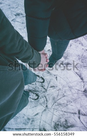Young pair holding their hand, ice skating on pond