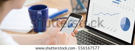 Close-up rear view of business woman working in office on pc holding smartphone and looking at screen with diagrams, using mobile phone and laptop. Horizontal photo banner for website header design