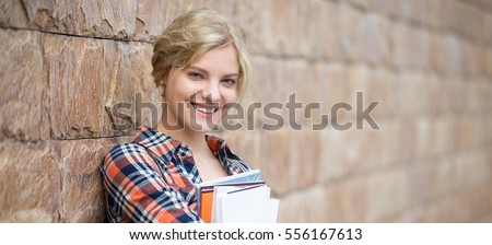 Portrait of a smiling attractive student with books against the brick wall. Back to school concept photo. Horizontal photo banner for website header design with copy space for text Royalty-Free Stock Photo #556167613