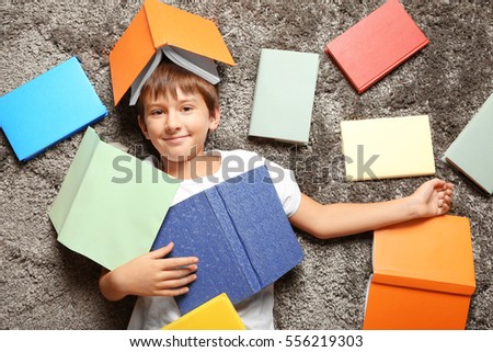 Cute schoolboy lying among books on carpet, top view