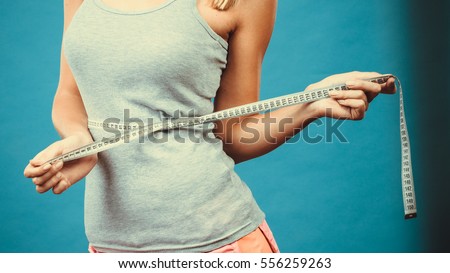 Weight loss, slim body, healthy lifestyle concept. Fit fitness girl measuring her waistline with measure tape on blue Royalty-Free Stock Photo #556259263