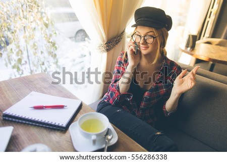 Young red hair hipster woman, making selfie, showing funny face, posing at cafe at winter day, stylish hat and clear sunglasses.

