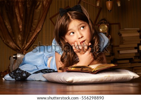 Little girl in blue dress lying on the floor in a room reading a book
