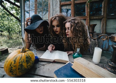 Three vintage witches perform magic ritual, at the table, reading a magical book on the eve of Halloween