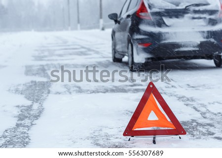 Transportation, winter and vehicle concept - closeup of red warning triangle with a broken down car