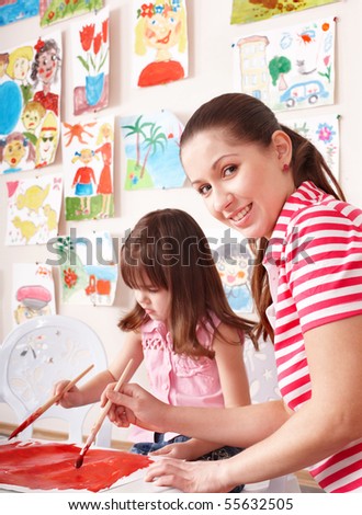 Little girl painting with teacher in preschool.