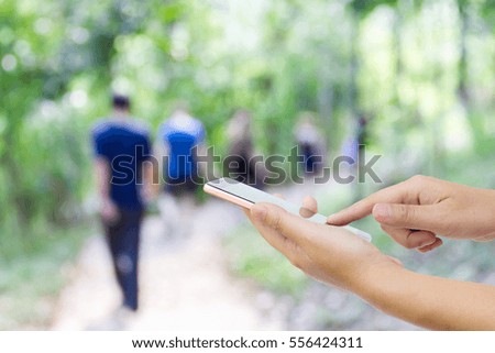 Man use mobile phone, blur image of tourists walk in the forest as background.