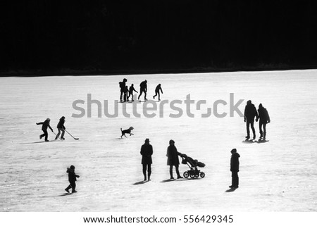 Young families enjoying themselves on a frozen lake having fun playing hockey and walking the pet dog silhouetted against the ice