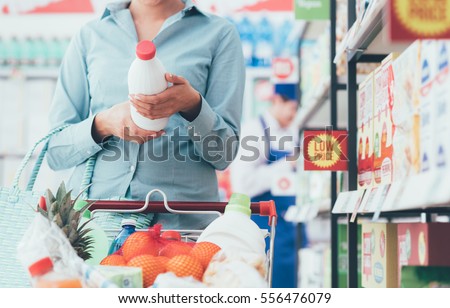 Woman doing grocery shopping at the supermarket and reading food labels, nutrition and quality concept Royalty-Free Stock Photo #556476079