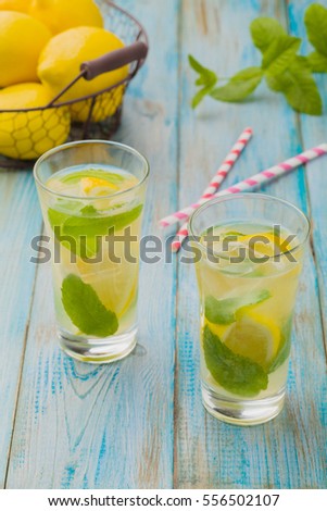 lemonade with mint and on rocks served in a glass with a straw on a wooden table.